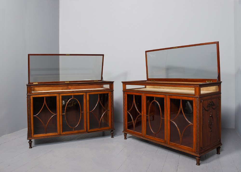 A pair of Adam style mahogany display counters featuring glass tops, glazed doors with geometric oval tracery, and carved swags on the sides. View II