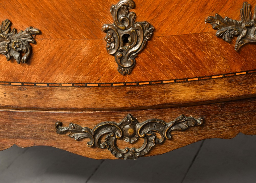 An antique French Louis XV style serpentine-fronted commode featuring three drawers with geometric wood inlay, cast brass handles, and a fitted beige marble top. View III