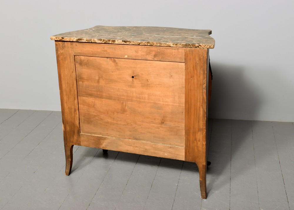 An antique French Louis XV style serpentine-fronted commode featuring three drawers with geometric wood inlay, cast brass handles, and a fitted beige marble top. View V