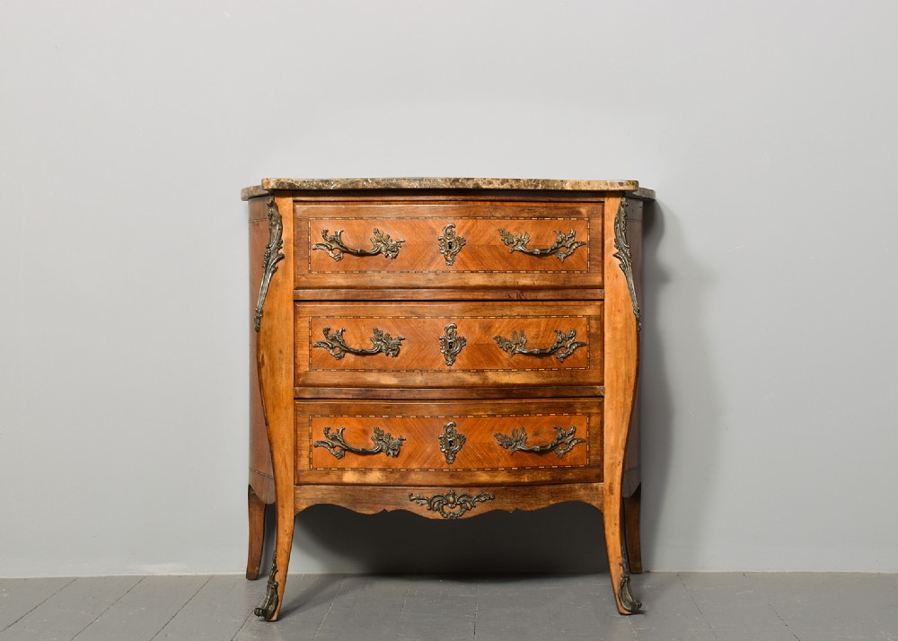 An antique French Louis XV style serpentine-fronted commode featuring three drawers with geometric wood inlay, cast brass handles, and a fitted beige marble top. View VIII