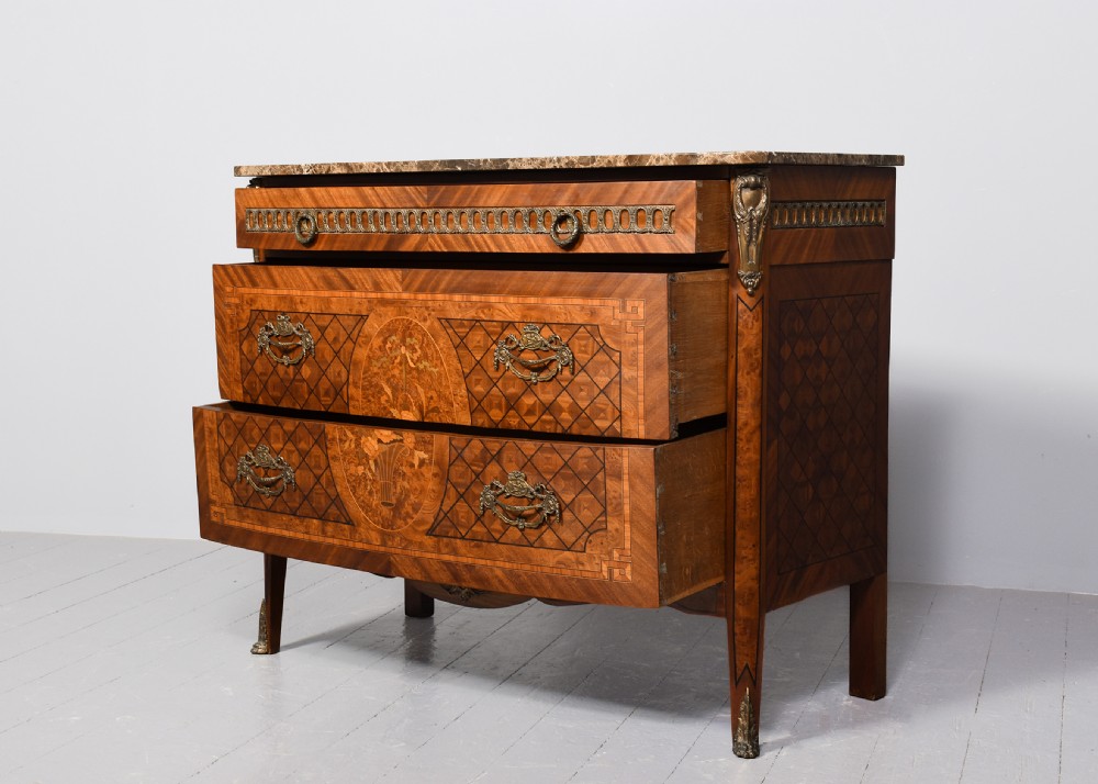 A French marquetry-inlaid walnut commode featuring three drawers, ornate brass hardware, and a brown veined marble top. View II