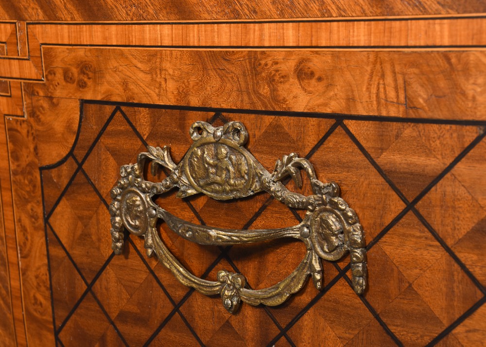 A French marquetry-inlaid walnut commode featuring three drawers, ornate brass hardware, and a brown veined marble top. View X