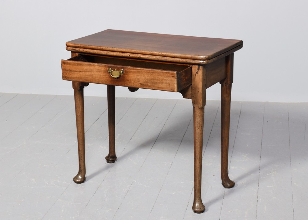 An 18th-century George II red walnut fold-over tea table with a single frieze drawer, brass brassware, shaped apron, and slender legs terminating in pad feet. View II