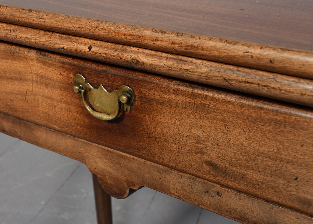 An 18th-century George II red walnut fold-over tea table with a single frieze drawer, brass brassware, shaped apron, and slender legs terminating in pad feet. View IV