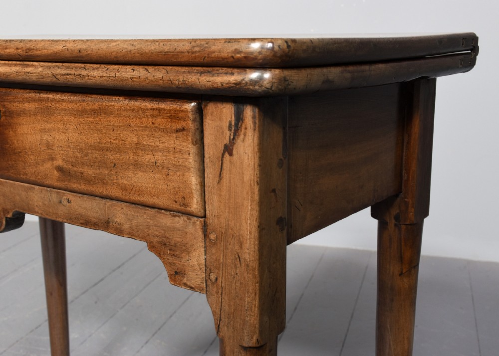 An 18th-century George II red walnut fold-over tea table with a single frieze drawer, brass brassware, shaped apron, and slender legs terminating in pad feet. View VI