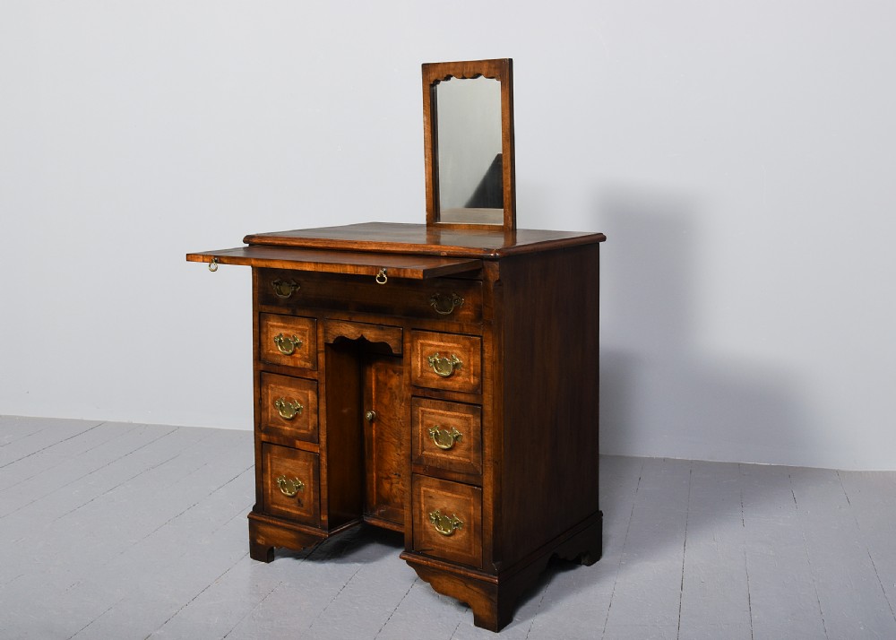 A George II style warm brown figured walnut kneehole dressing chest with brass drop handles, a pull-out slide, and a rectangular dressing mirror.