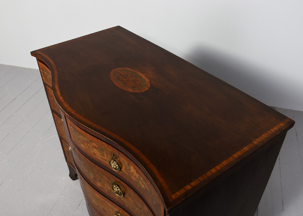 A George III style serpentine front chest of drawers featuring satinwood and floral marquetry inlay with brass ring handles. View II