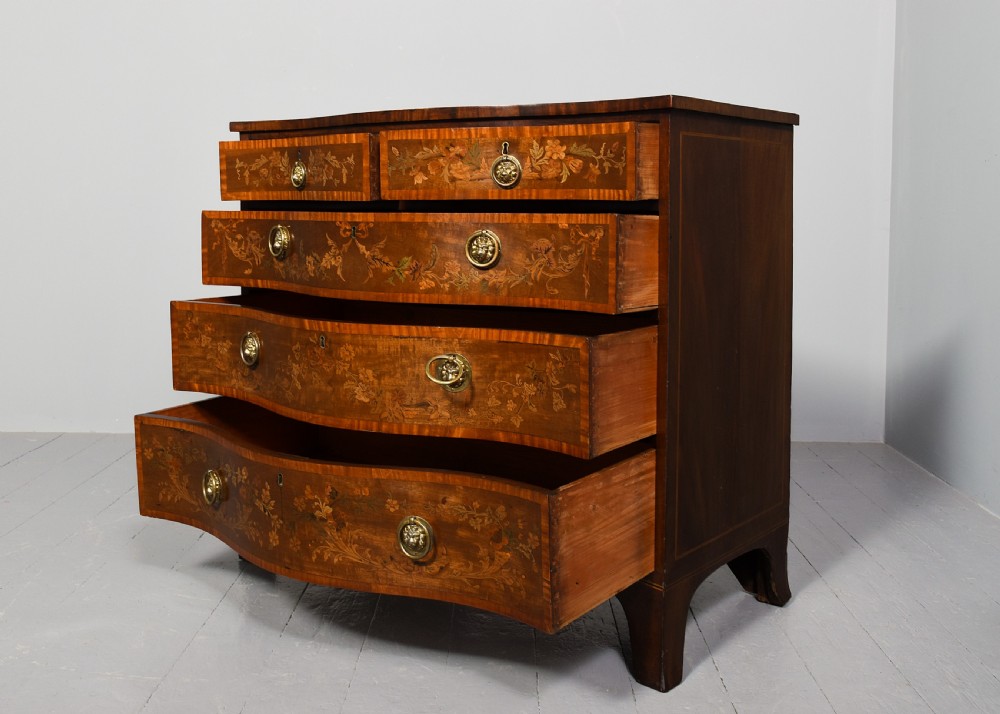 A George III style serpentine front chest of drawers featuring satinwood and floral marquetry inlay with brass ring handles. View IV