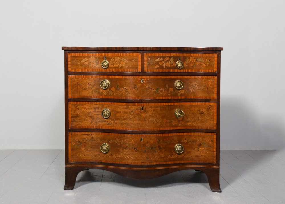 A George III style serpentine front chest of drawers featuring satinwood and floral marquetry inlay with brass ring handles. View V
