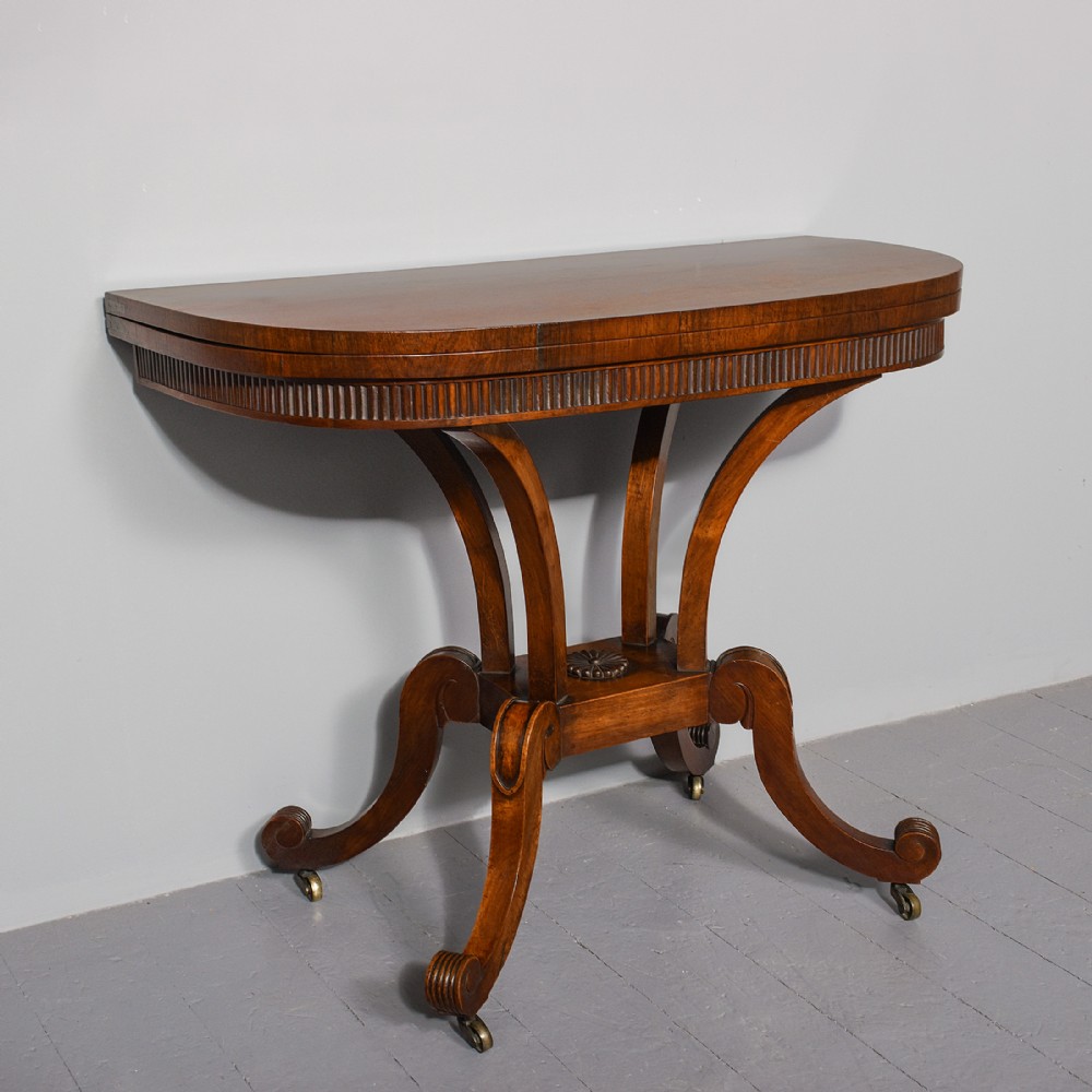 A Regency rosewood D-shaped fold-over tea table featuring a reeded apron, quadform curved legs, and brass castors on a grey floor.