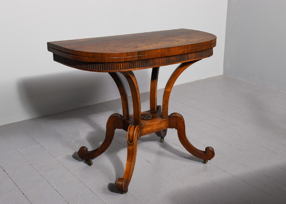 A Regency rosewood D-shaped fold-over tea table featuring a reeded apron, quadform curved legs, and brass castors on a grey floor. View II