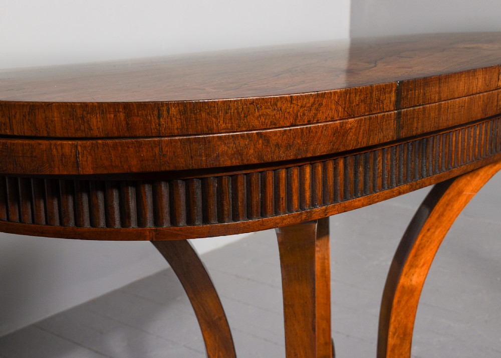 A Regency rosewood D-shaped fold-over tea table featuring a reeded apron, quadform curved legs, and brass castors on a grey floor. View III