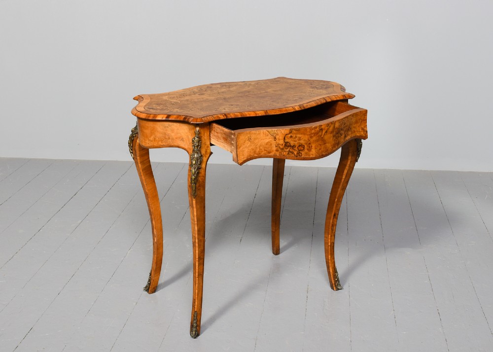 A Victorian burr walnut side table featuring a serpentine shaped top, gilt-bronze mounts, and carved cabriole legs. View II