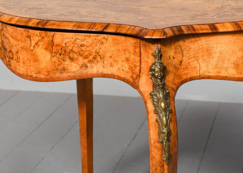 A Victorian burr walnut side table featuring a serpentine shaped top, gilt-bronze mounts, and carved cabriole legs. View IV