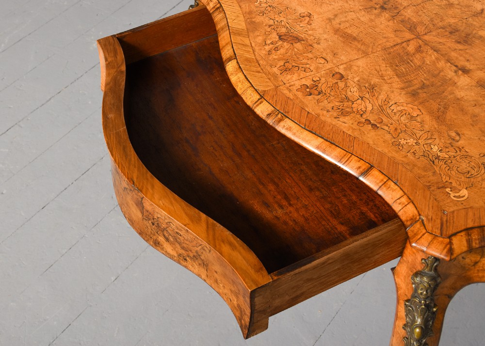 A Victorian burr walnut side table featuring a serpentine shaped top, gilt-bronze mounts, and carved cabriole legs. View VI