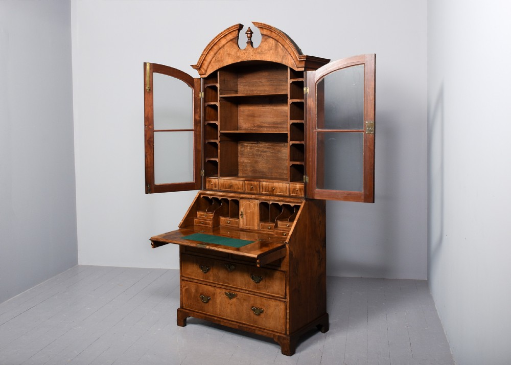 A George II walnut bureau bookcase featuring a broken arch pediment with finial, glazed upper doors, a fall-front desk, and lower drawers on bracket feet. View II