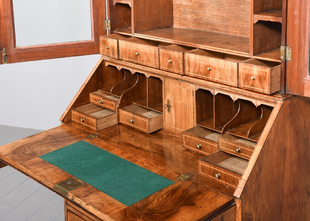 A George II walnut bureau bookcase featuring a broken arch pediment with finial, glazed upper doors, a fall-front desk, and lower drawers on bracket feet. View III