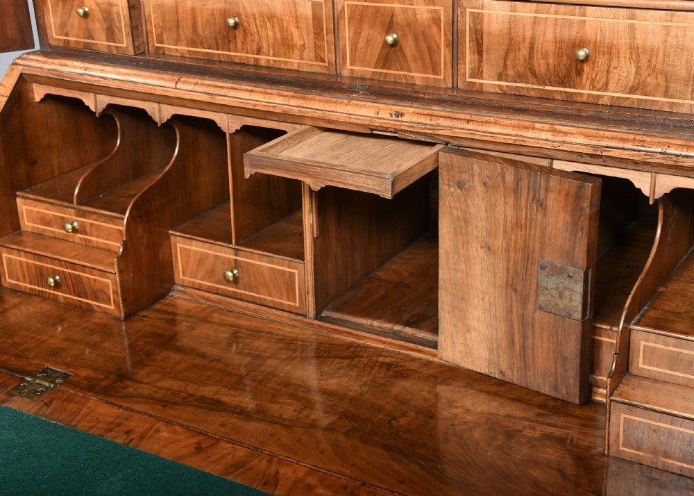 A George II walnut bureau bookcase featuring a broken arch pediment with finial, glazed upper doors, a fall-front desk, and lower drawers on bracket feet. View IV