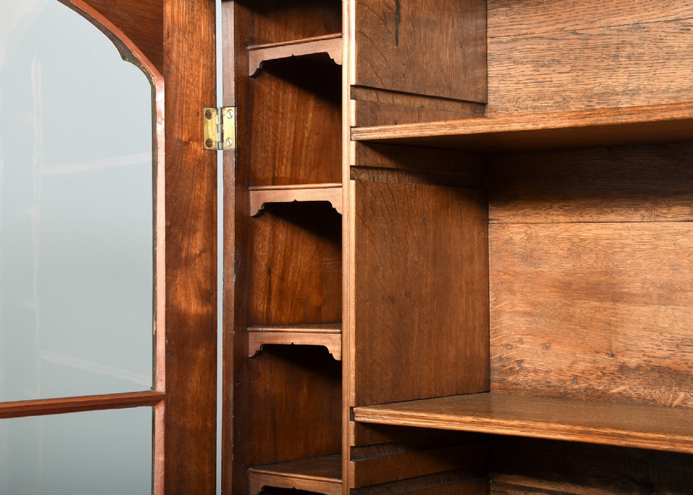 A George II walnut bureau bookcase featuring a broken arch pediment with finial, glazed upper doors, a fall-front desk, and lower drawers on bracket feet. View V