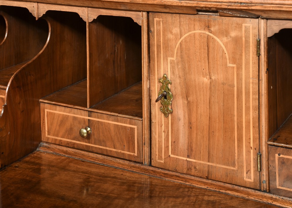 A George II walnut bureau bookcase featuring a broken arch pediment with finial, glazed upper doors, a fall-front desk, and lower drawers on bracket feet. View VI