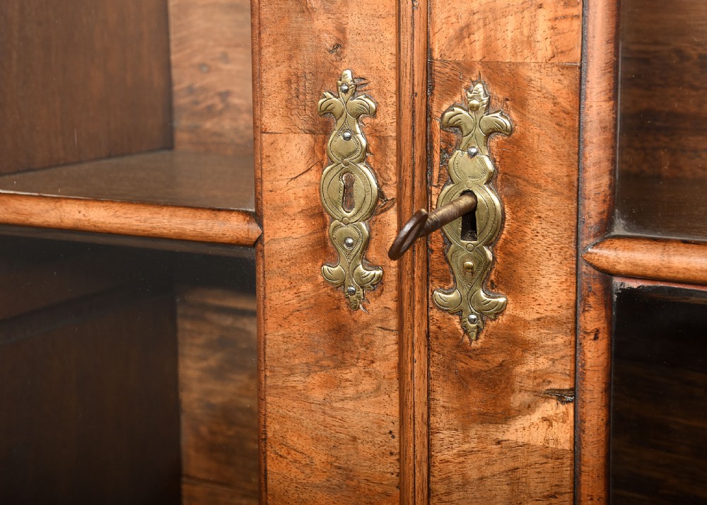 A George II walnut bureau bookcase featuring a broken arch pediment with finial, glazed upper doors, a fall-front desk, and lower drawers on bracket feet. View VII