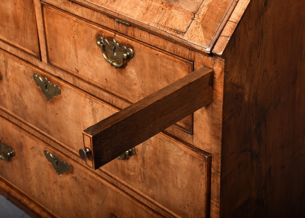 A George II walnut bureau bookcase featuring a broken arch pediment with finial, glazed upper doors, a fall-front desk, and lower drawers on bracket feet. View IX