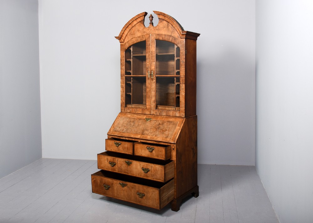 A George II walnut bureau bookcase featuring a broken arch pediment with finial, glazed upper doors, a fall-front desk, and lower drawers on bracket feet. View XI