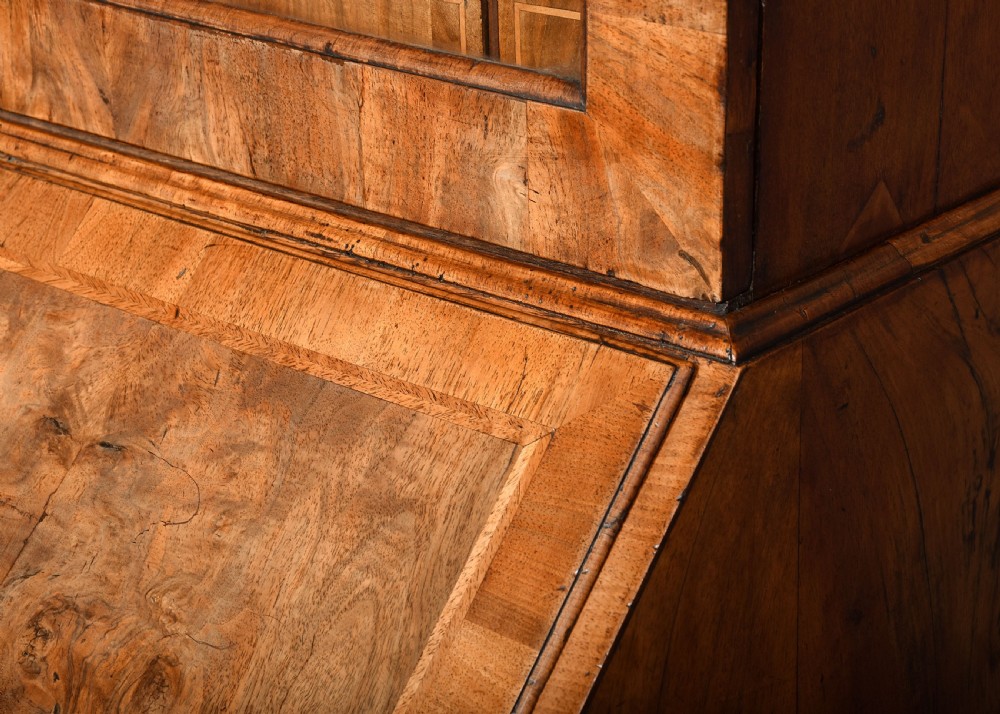 A George II walnut bureau bookcase featuring a broken arch pediment with finial, glazed upper doors, a fall-front desk, and lower drawers on bracket feet. View XVII
