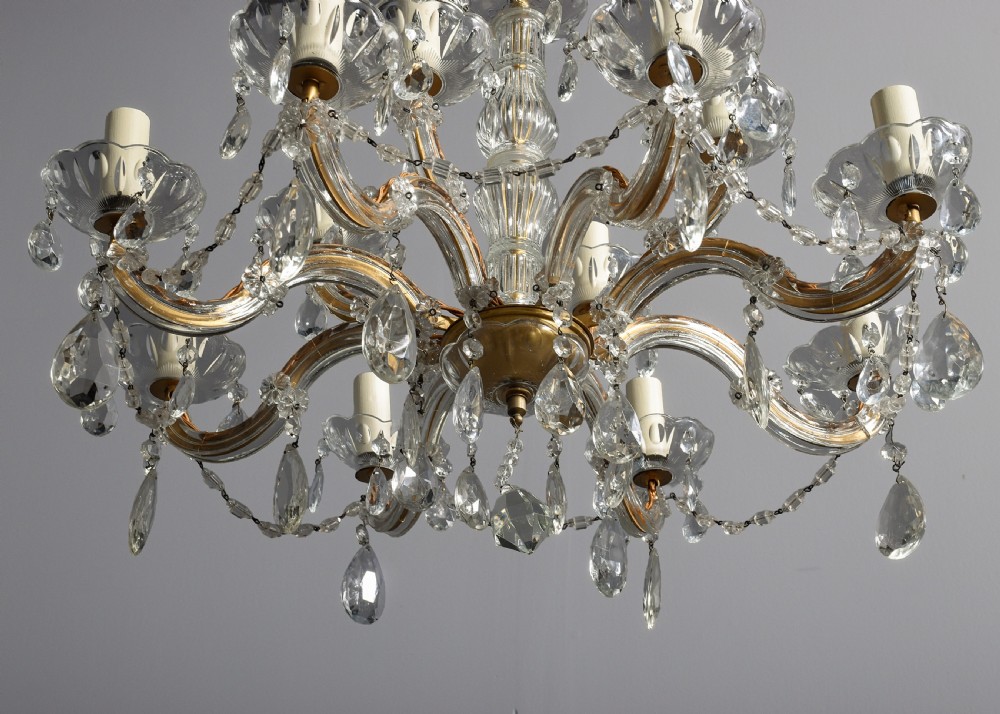 A multi-arm clear glass and cut crystal chandelier featuring hanging teardrop prisms, scalloped glass candle cups, and white candle sleeves. View IV