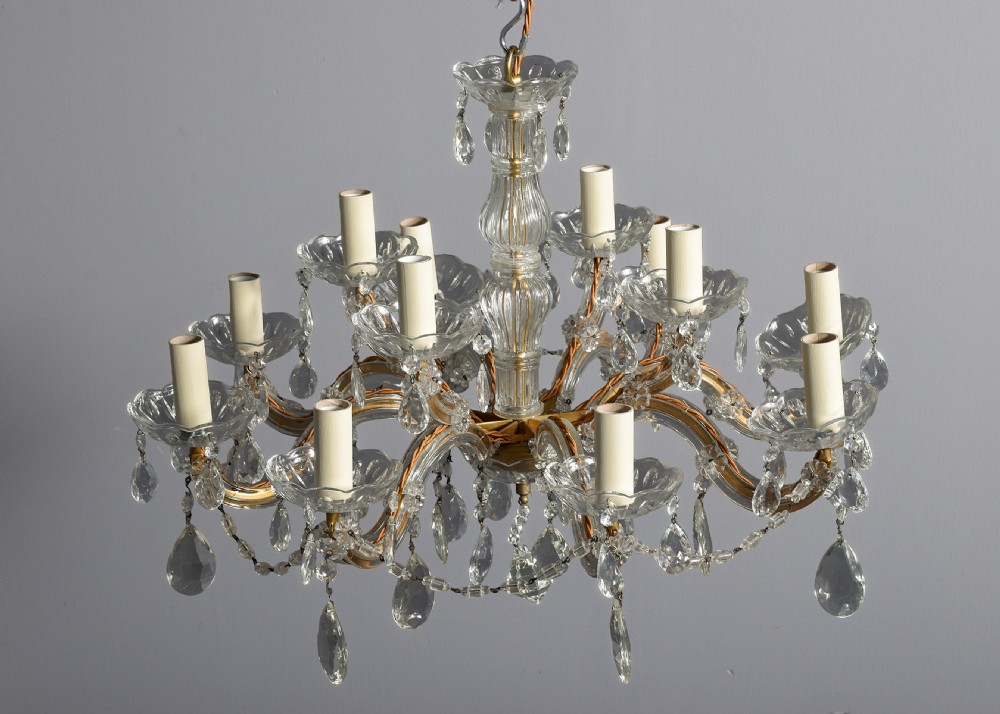 A multi-arm clear glass and cut crystal chandelier featuring hanging teardrop prisms, scalloped glass candle cups, and white candle sleeves. View VII