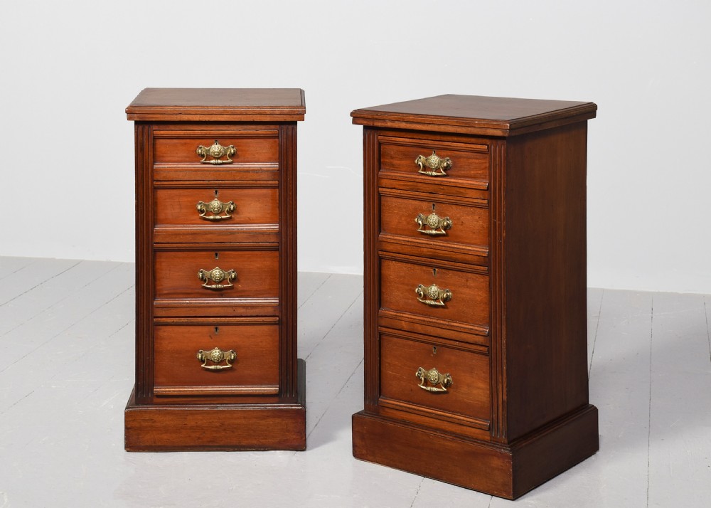A pair of narrow late Victorian walnut bedside lockers with four drawers, brass drop handles, keyholes, and solid plinth bases.