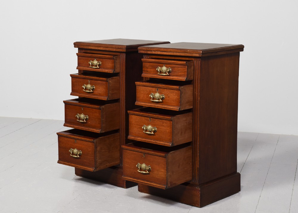 A pair of narrow late Victorian walnut bedside lockers with four drawers, brass drop handles, keyholes, and solid plinth bases. View II