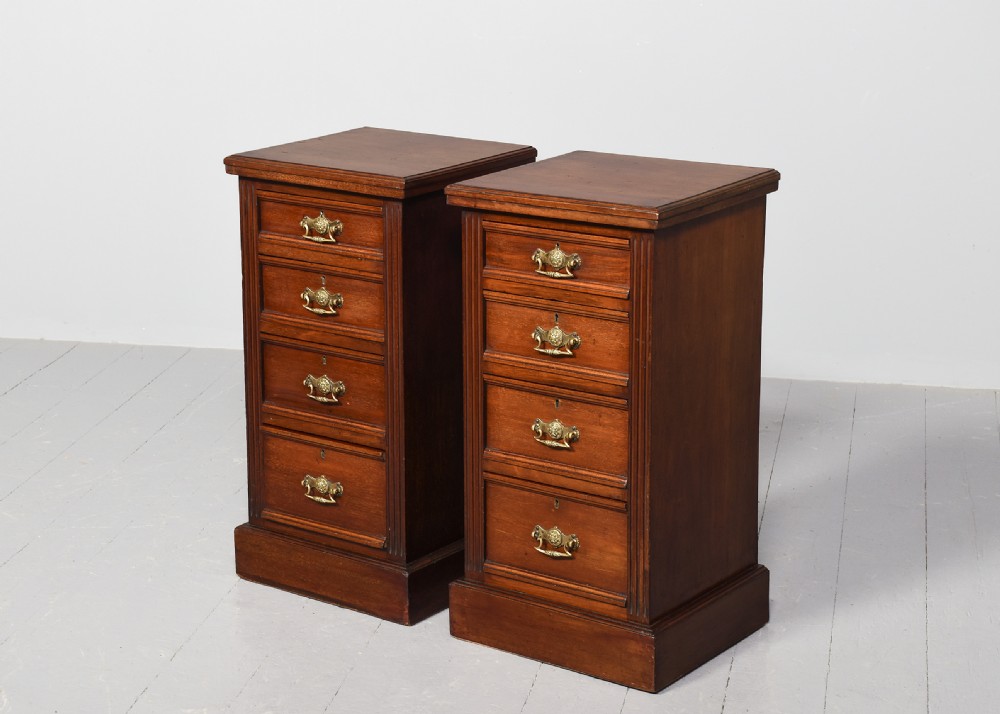 A pair of narrow late Victorian walnut bedside lockers with four drawers, brass drop handles, keyholes, and solid plinth bases. View III