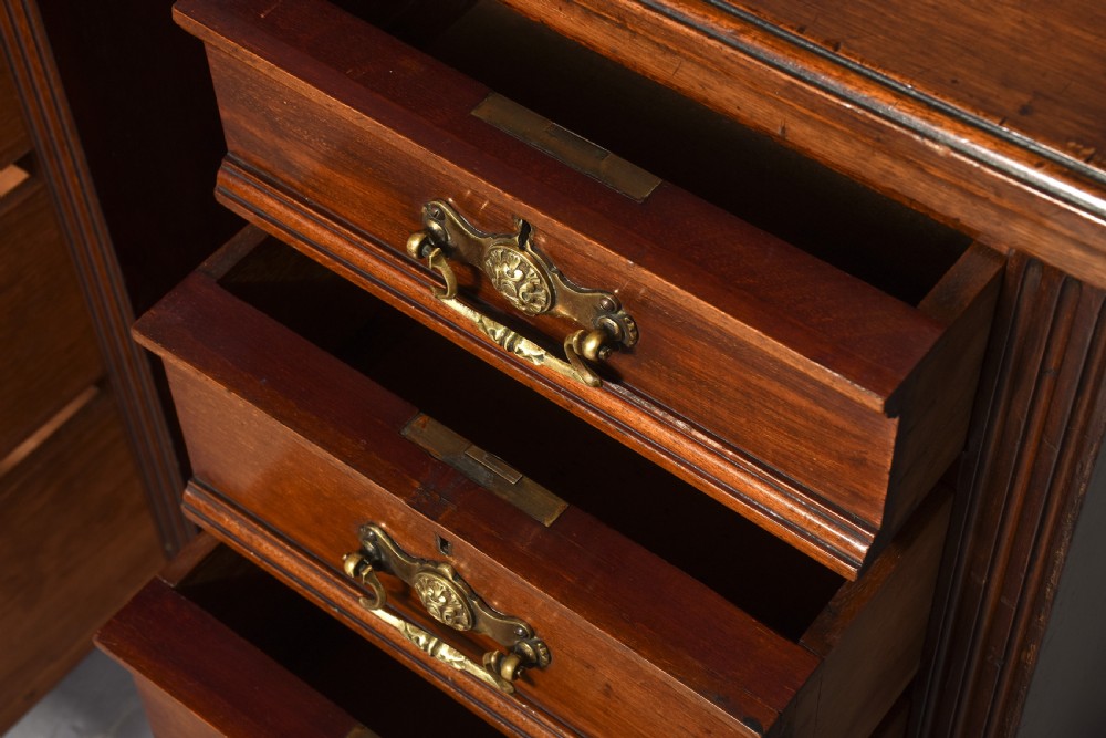 A pair of narrow late Victorian walnut bedside lockers with four drawers, brass drop handles, keyholes, and solid plinth bases. View IV