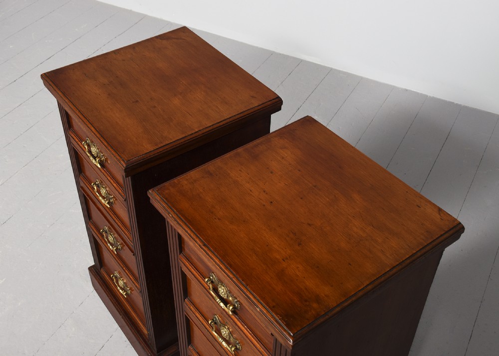 A pair of narrow late Victorian walnut bedside lockers with four drawers, brass drop handles, keyholes, and solid plinth bases. View V