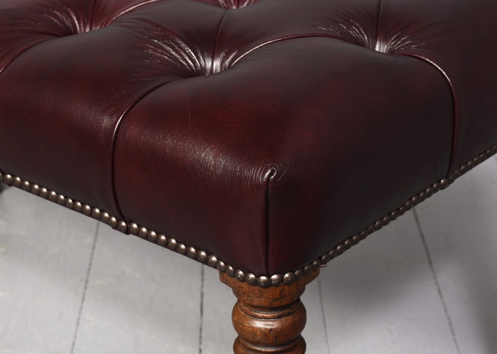 A pair of rectangular mahogany long stools upholstered in deep-buttoned burgundy leather with brass stud borders and fluted turned legs. View II