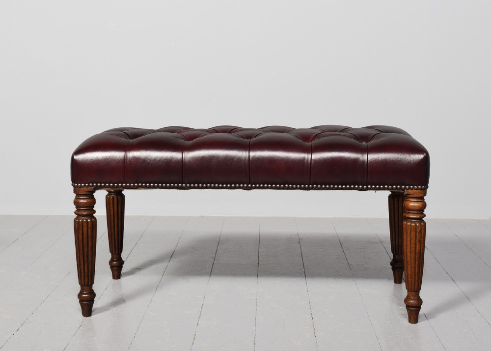 A pair of rectangular mahogany long stools upholstered in deep-buttoned burgundy leather with brass stud borders and fluted turned legs. View III