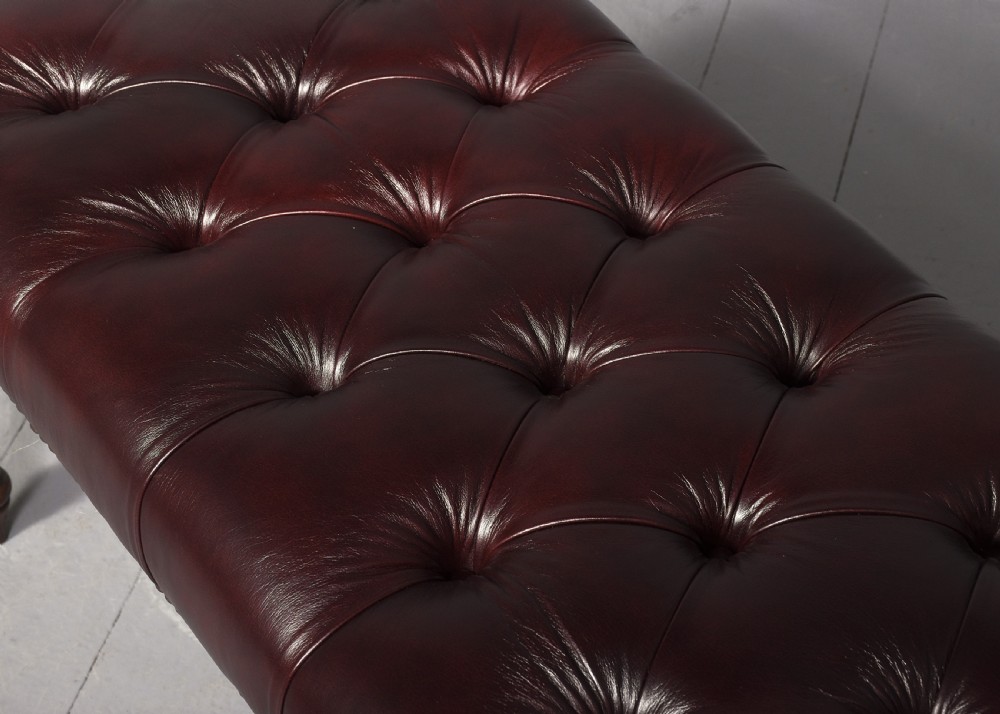 A pair of rectangular mahogany long stools upholstered in deep-buttoned burgundy leather with brass stud borders and fluted turned legs. View IV