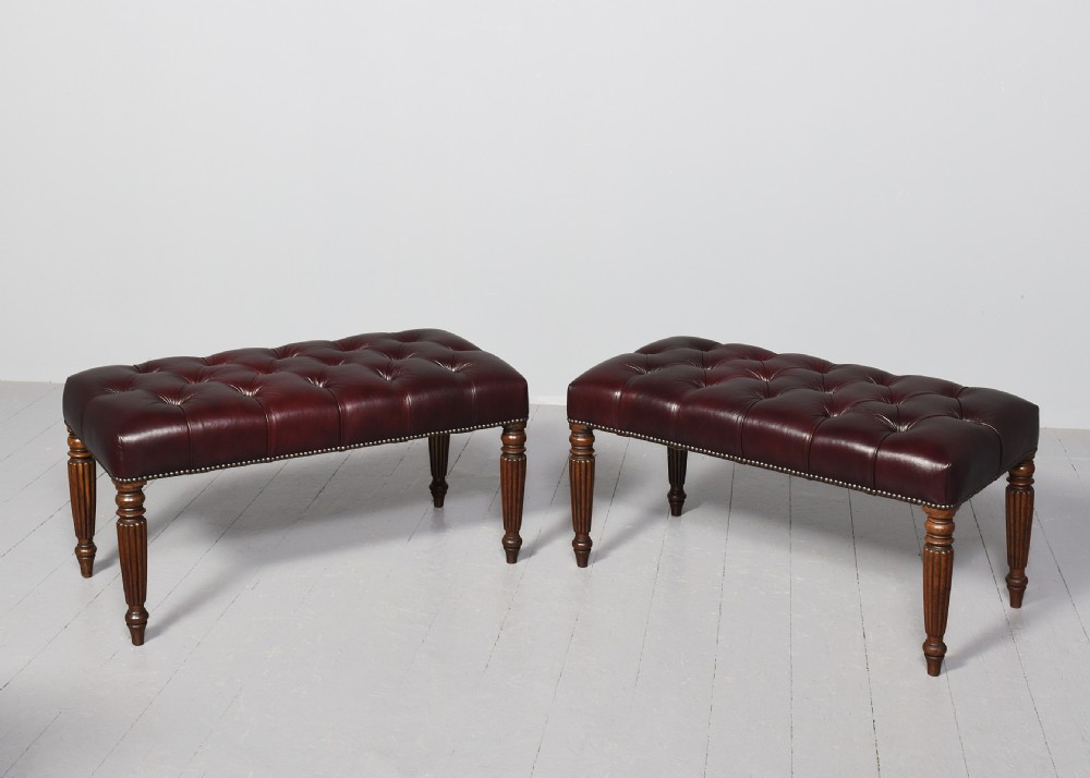 A pair of rectangular mahogany long stools upholstered in deep-buttoned burgundy leather with brass stud borders and fluted turned legs. View V