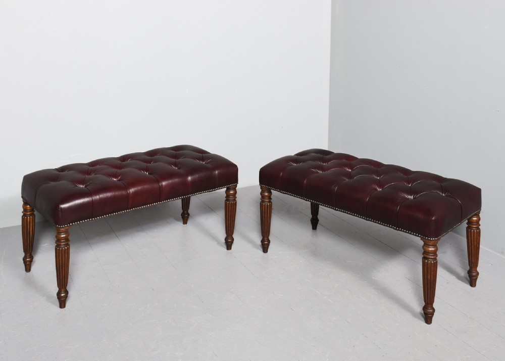 A pair of rectangular mahogany long stools upholstered in deep-buttoned burgundy leather with brass stud borders and fluted turned legs. View VI