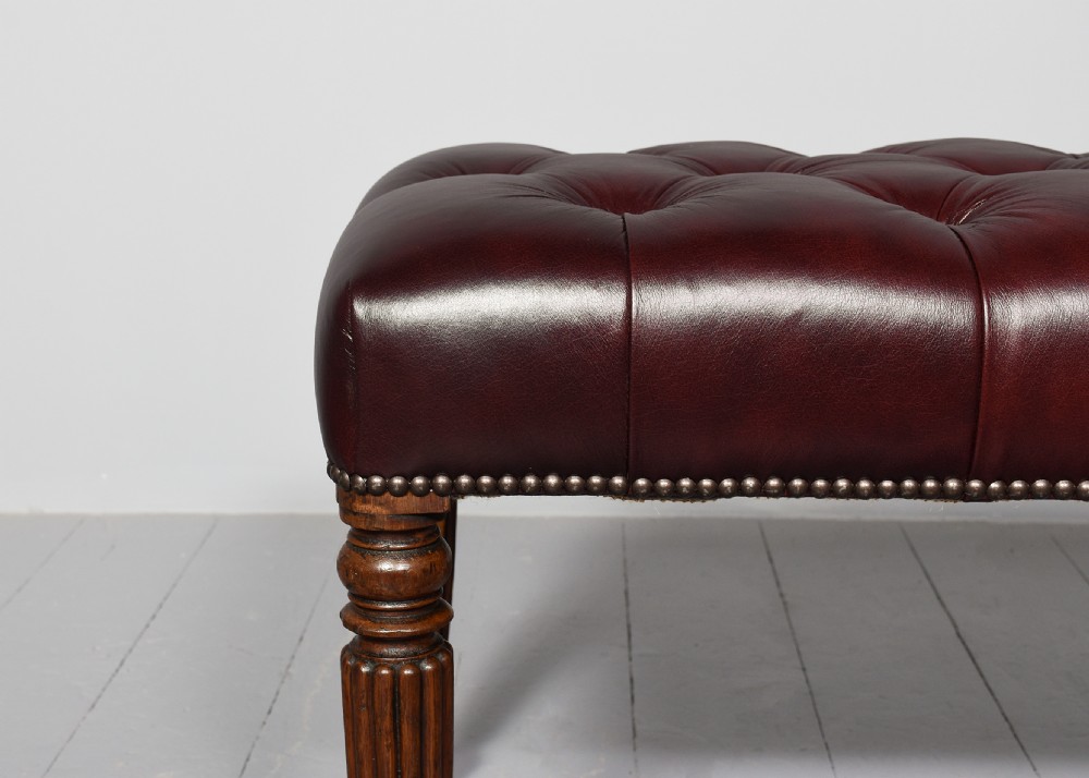 A pair of rectangular mahogany long stools upholstered in deep-buttoned burgundy leather with brass stud borders and fluted turned legs. View VII