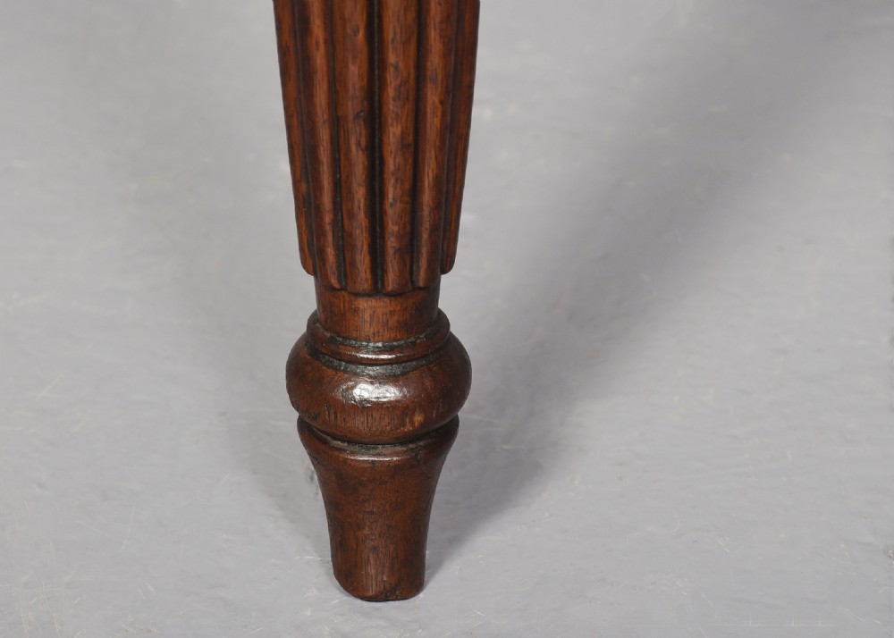 A pair of rectangular mahogany long stools upholstered in deep-buttoned burgundy leather with brass stud borders and fluted turned legs. View VIII