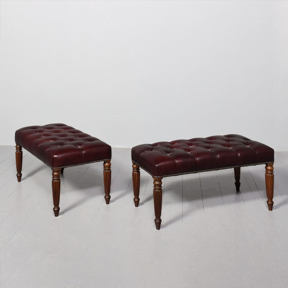 A pair of rectangular mahogany long stools upholstered in deep-buttoned burgundy leather with brass stud borders and fluted turned legs. View IX