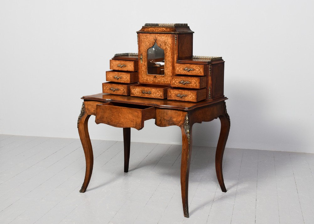 A Victorian figured walnut bonheur de jour writing desk featuring marquetry inlays, a mirrored central cabinet, brass gallery rail, and slender cabriole legs. View II