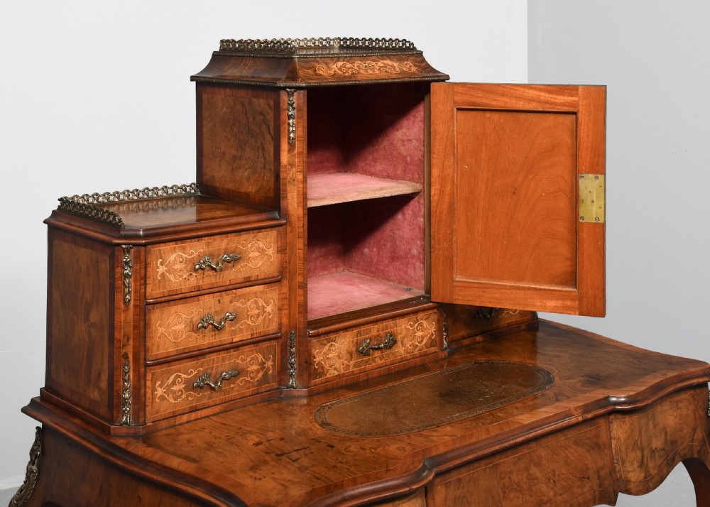 A Victorian figured walnut bonheur de jour writing desk featuring marquetry inlays, a mirrored central cabinet, brass gallery rail, and slender cabriole legs. View IV