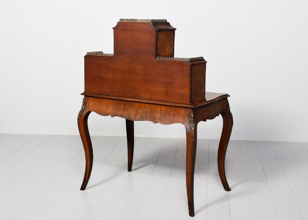 A Victorian figured walnut bonheur de jour writing desk featuring marquetry inlays, a mirrored central cabinet, brass gallery rail, and slender cabriole legs. View IX
