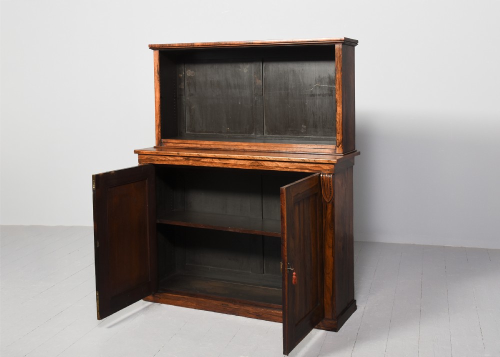 A two-part Regency rosewood bookcase featuring an open upper shelf area above a twin-door lower cupboard with carved corbels. View II
