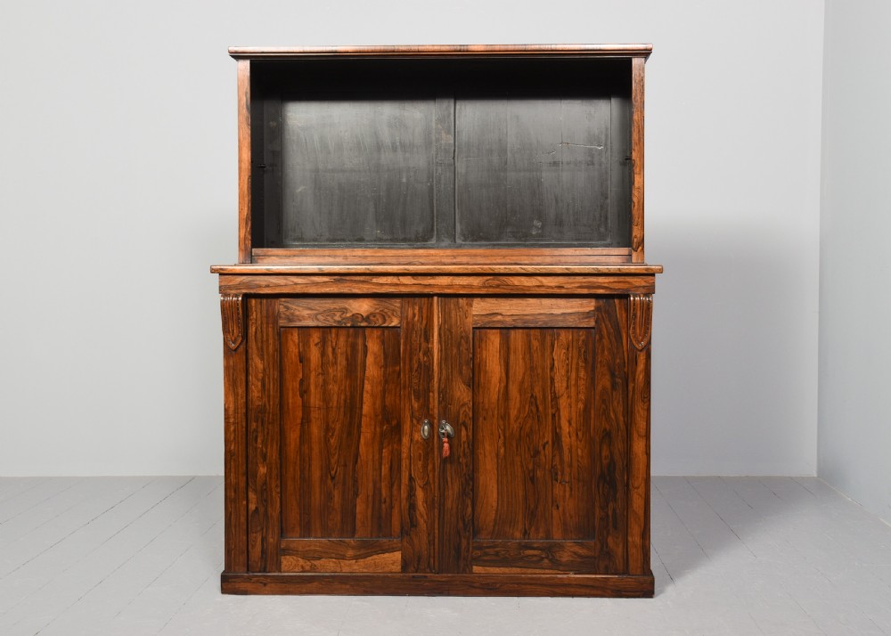 A two-part Regency rosewood bookcase featuring an open upper shelf area above a twin-door lower cupboard with carved corbels. View VII