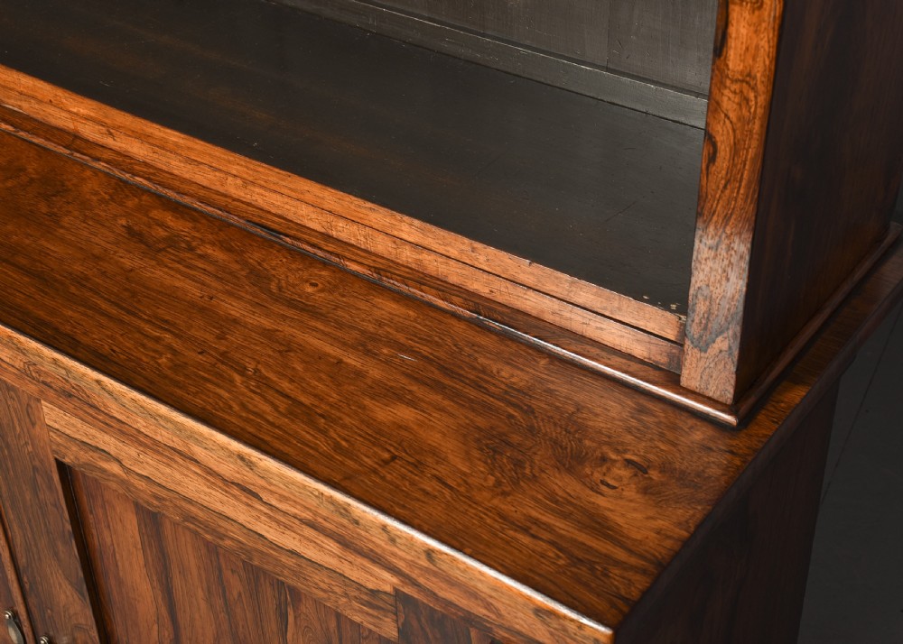 A two-part Regency rosewood bookcase featuring an open upper shelf area above a twin-door lower cupboard with carved corbels. View X