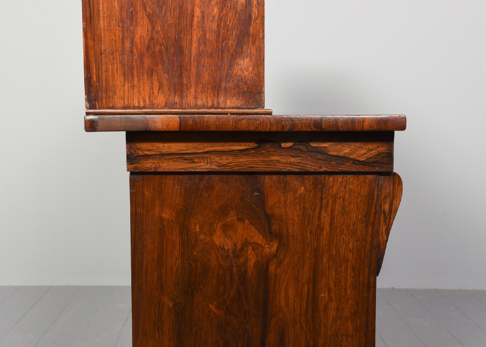A two-part Regency rosewood bookcase featuring an open upper shelf area above a twin-door lower cupboard with carved corbels. View XII